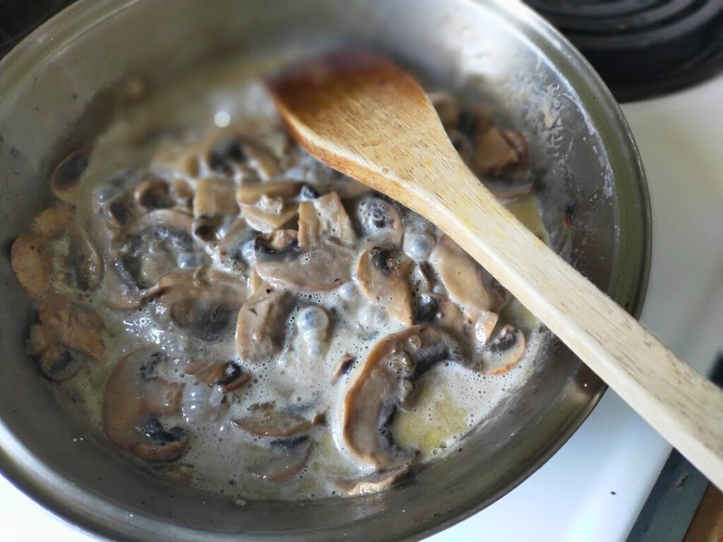 mushrooms cooking in cream and butter to make a delicious sauce. in a pot with wooden spoon