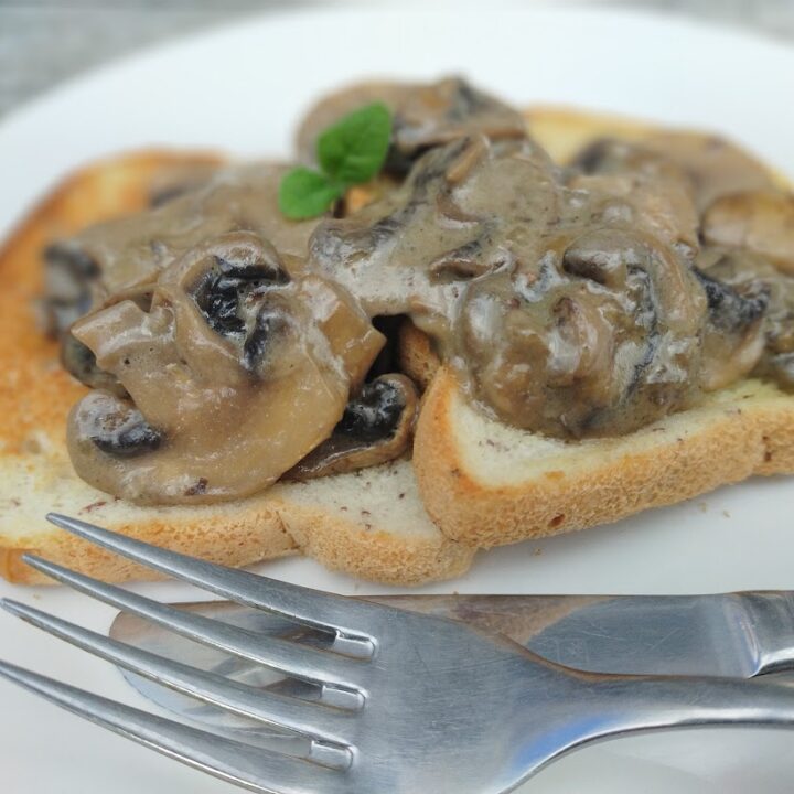 Creamy mushrooms served on toast sitting on a plate with knife and fork