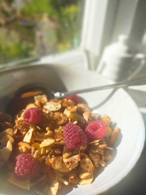 Maple granola served in a bowl with raspberries sitting on window sill