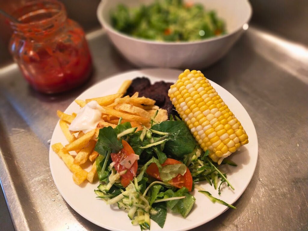 Main meal served on a plate with fries, corn on the cob, salad and meat.