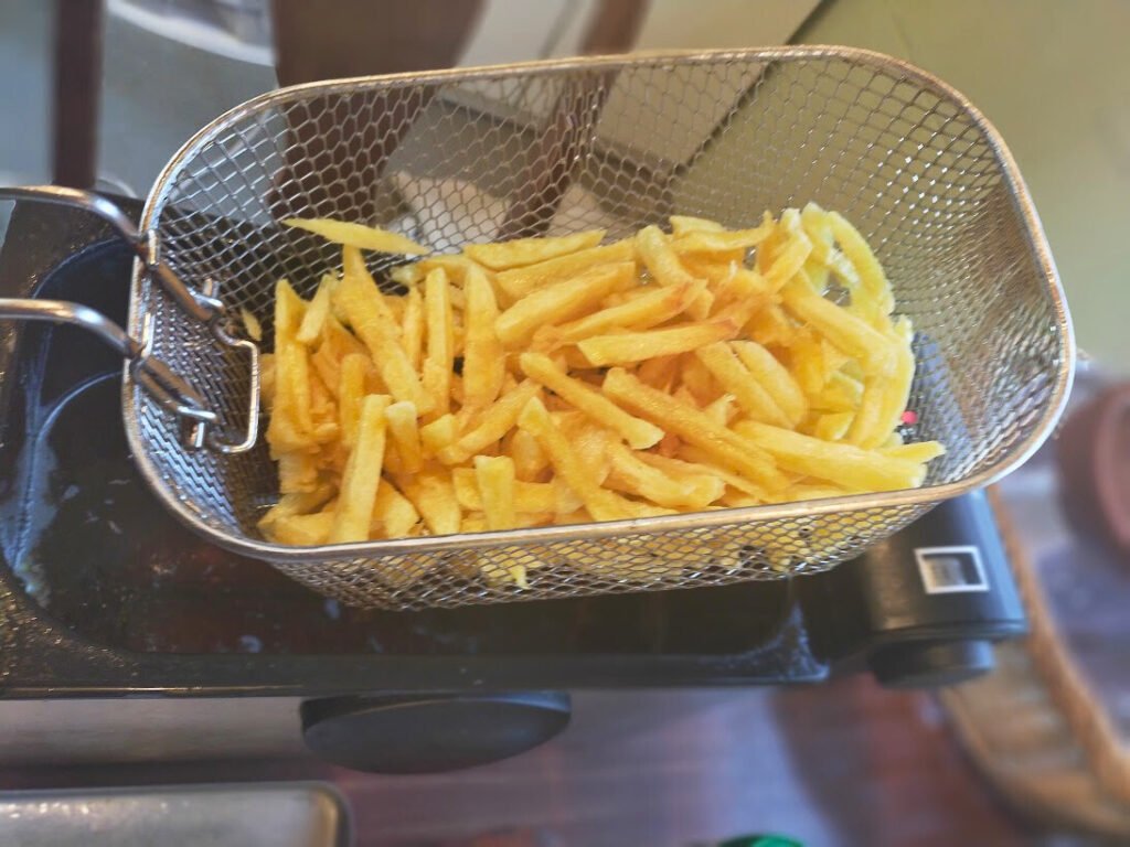 Cooked fries in a deep fryer basket draining off the oil.