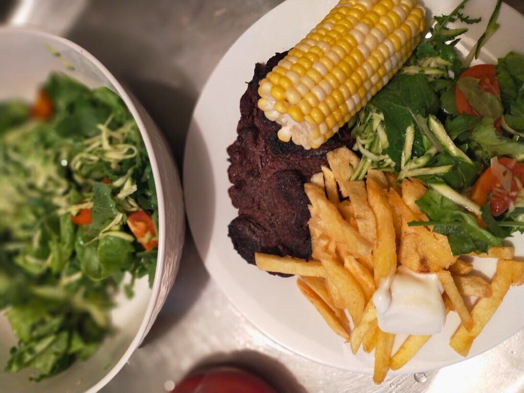 Homemade fries served on a plate with stead, corn and salad. Bowl of salad beside.