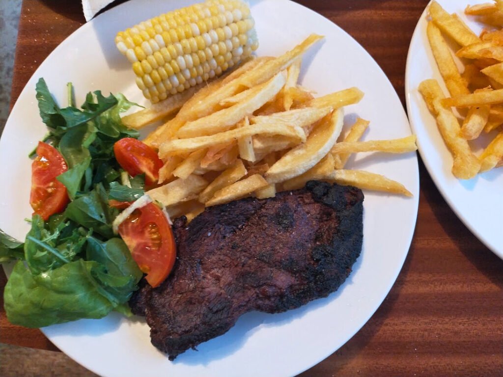 Steak, homemade fries, salad and corn served on a plate