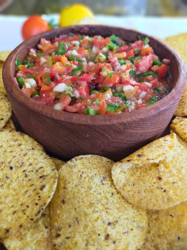 Fresh tomato and green pepper salsa served in a wooden bowl with corn chips