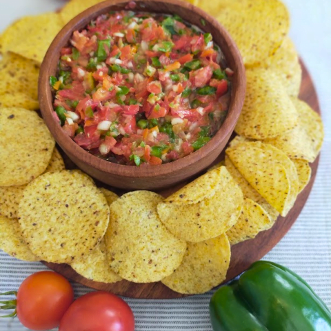 Tomato and green pepper salsa in wooden bowl served with corn chips