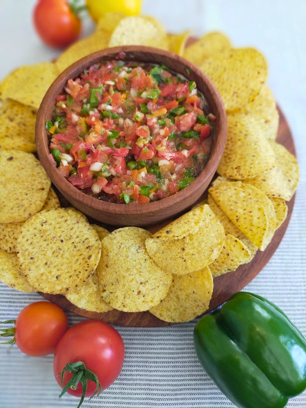 Fresh tomato and green pepper salsa served in a wooden bowl with a platter of corn chips