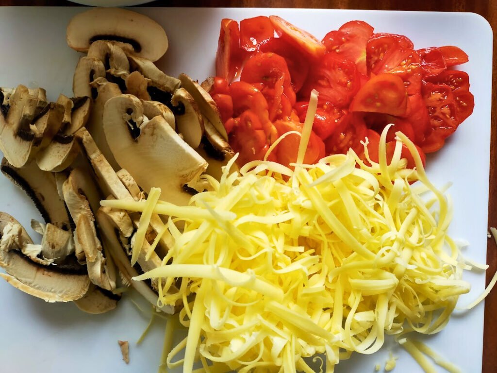 sliced tomato and mushroom on a chopping board with grated cheese