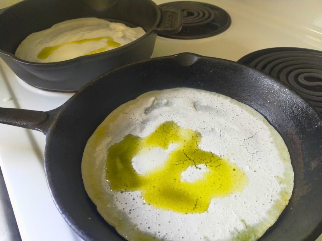 Pizza base in a cast-iron skillet with olive oil ready to bake.