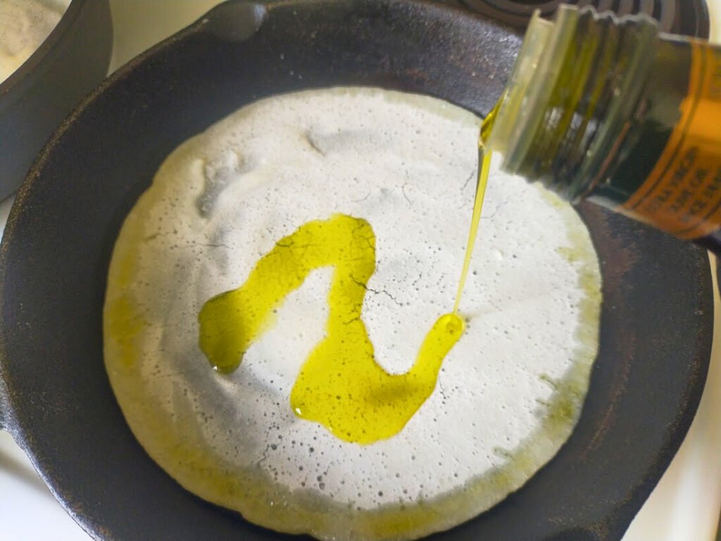 drizzling olive oil over a pizza base in a cast-iron skillet