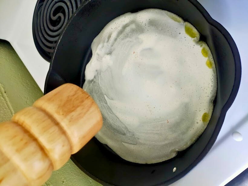 salt grinder over pizza base in a cast-iron skillet