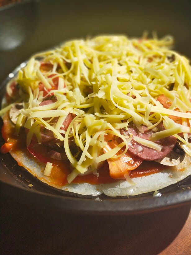 grated cheese on top of other pizza toppings in a cast-iron skillet