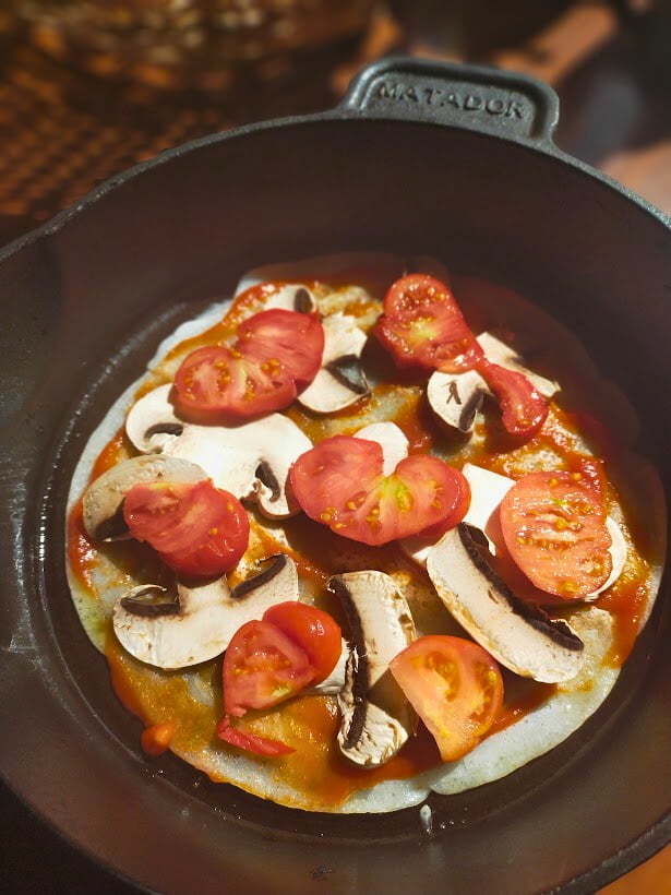 sliced tomato and mushroom on a pizza base in a cast-iron skillet.