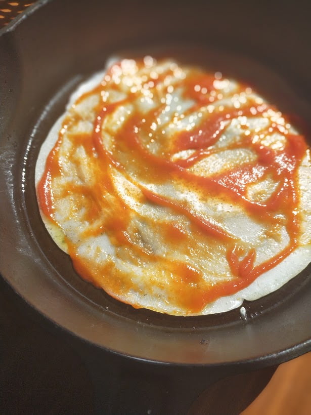 pizza base in a cast-iron skillet with tomato sauce spread over the top.