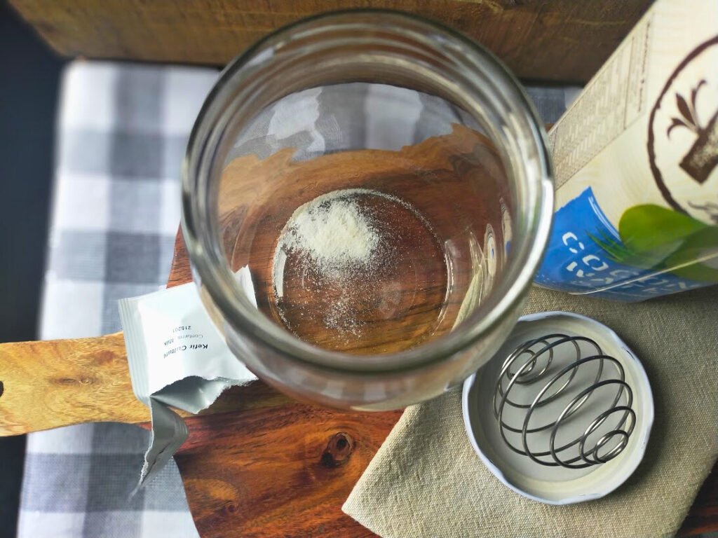 Kefir culture in a glass jar sitting beside a bottle and a mixing ball