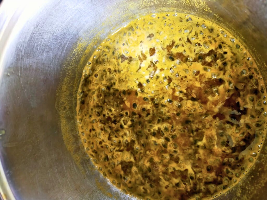 Passionfruit pulp and sugar cooking in a pot.