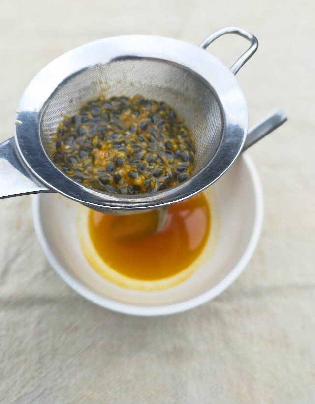 Straining the seeds out of the passionfruit syrup with a sieve.