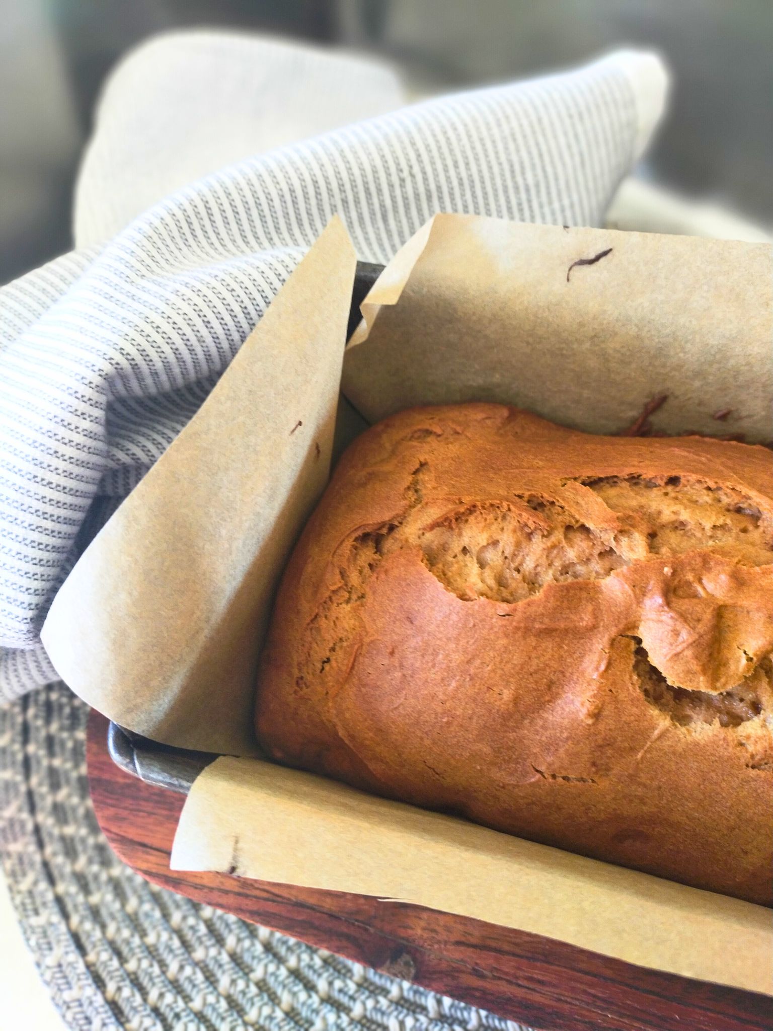 Baked Gluten free gingerbread loaf in the tin on a wooden board with a blue and white tea towel in the background