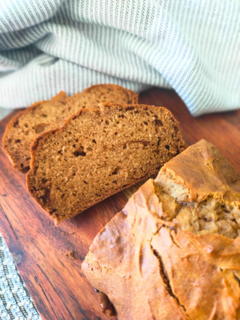 Baked gingerbread loaf, sliced on a wooden board with a blue and white tea towel in the background.