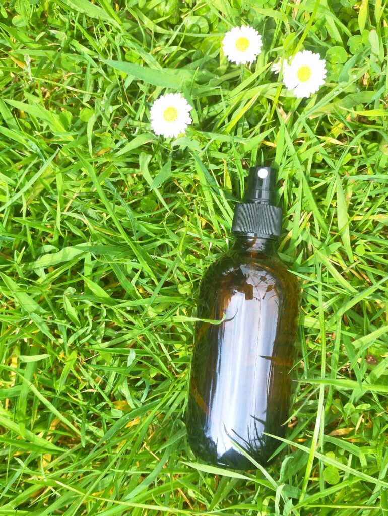 Amber glass bottle with spray lid lying on the grass with 3 white daisies ready to make essential oil perfume spray.