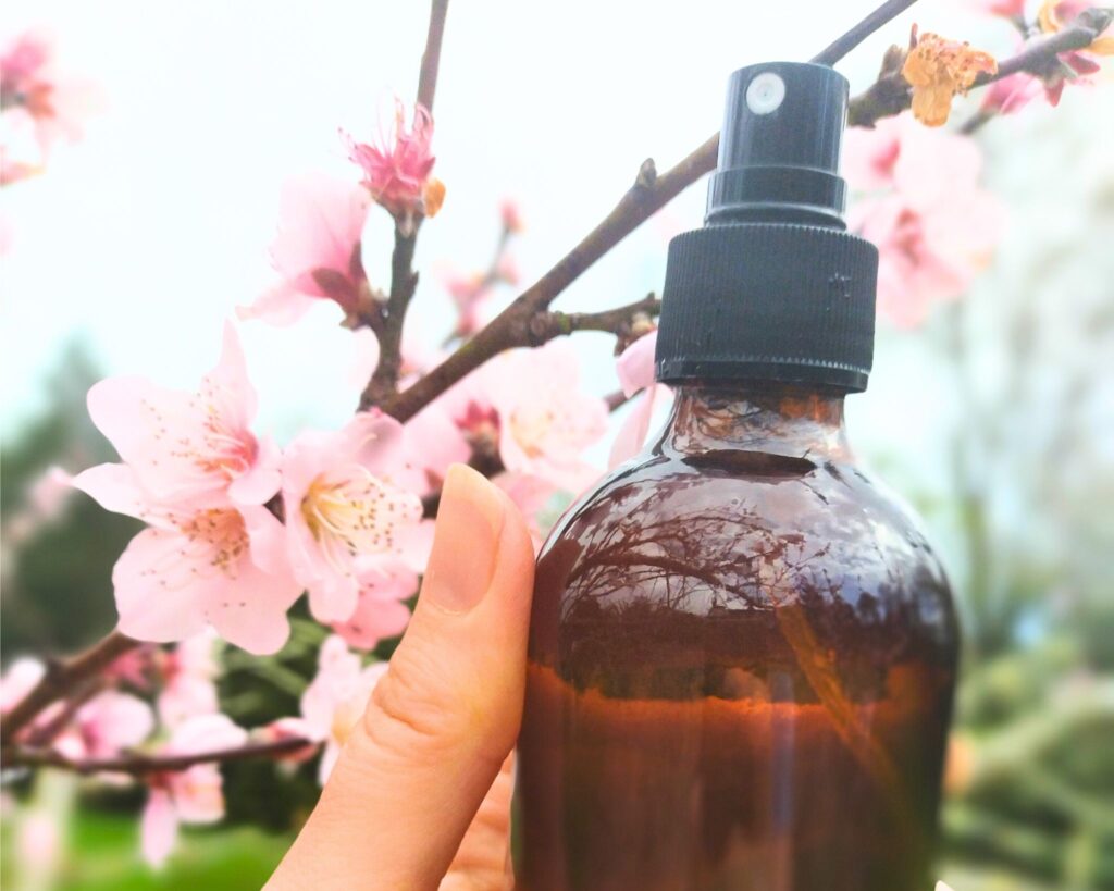 Natural Air-freshener in an amber spray bottle being held in front of a blossom tree outside.