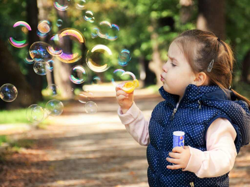 Little girl blowing bubbles while outside in the trees.