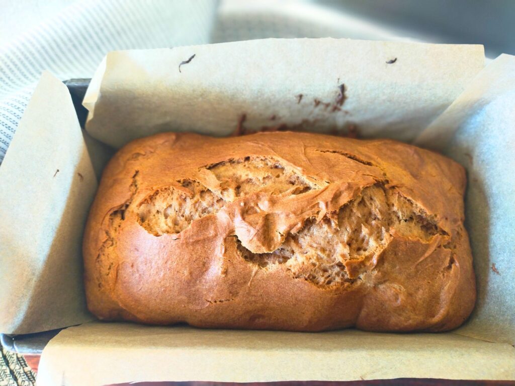 Freshly baked Gingerbread loaf still in the lined loaf tin with a tea towel in the background.