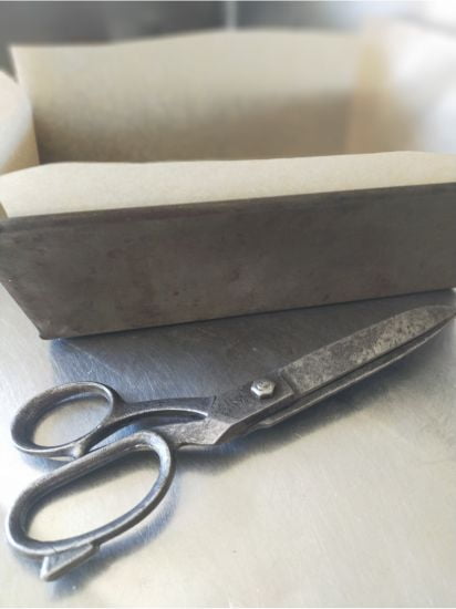 Loaf tin lined with baking paper sitting on a bench with old scissors in the the foreground