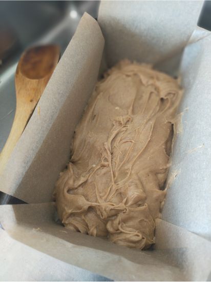 Lined loaf tin with the batter spread inside sitting next to a wooden spoon on the bench
