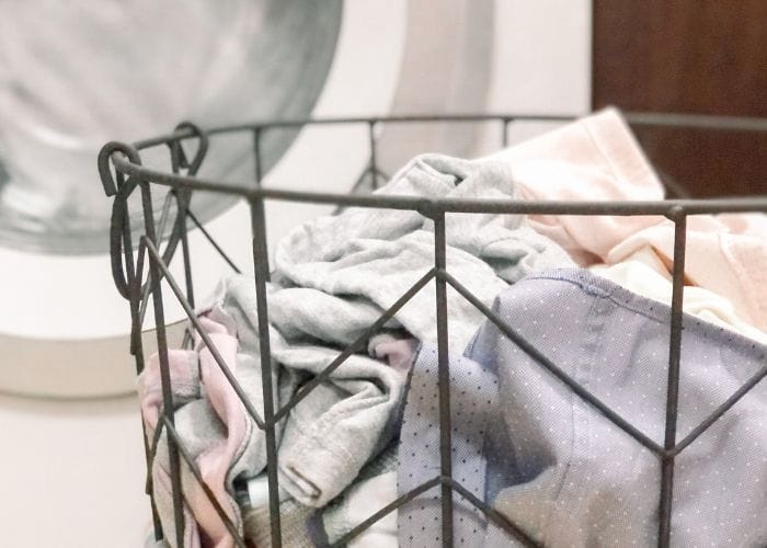 Wire laundry basket fill of clothing sitting in front of a washing machine