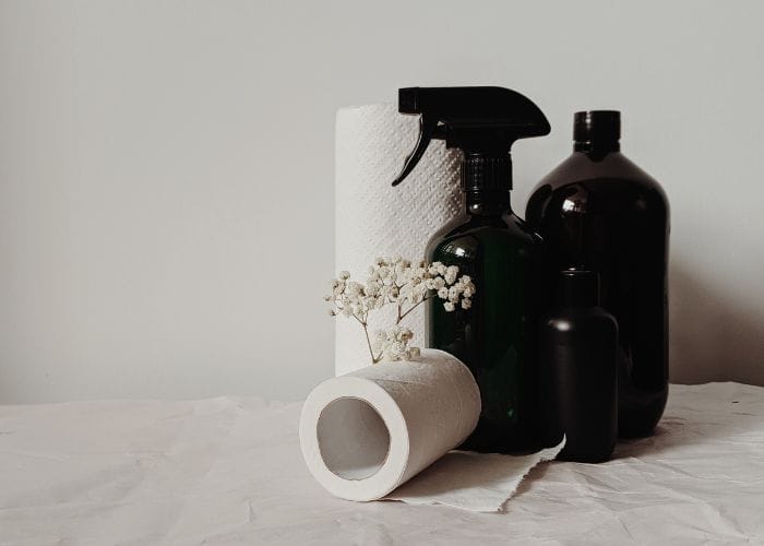 All natural laundry products in glass bottles sitting on a bench with rolls of paper towels