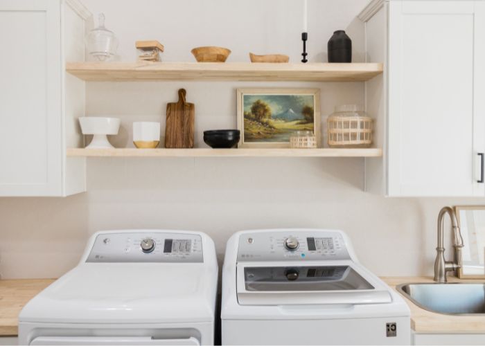 washing machine and tumble dryer sitting in a laundry room under an open shelf with wooden items on display