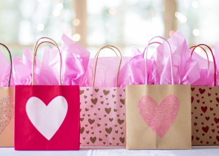 Several gift bags with love hearts on them stuffed with pink tissue paper.
