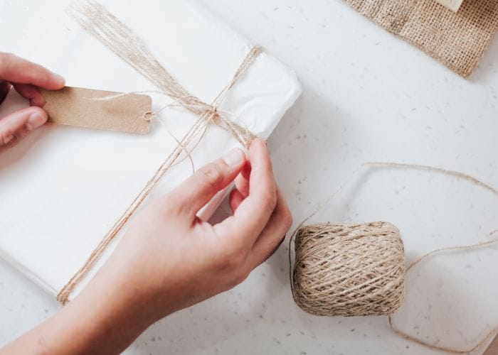 Tying a gift with white paper with brown string ready to give to someone