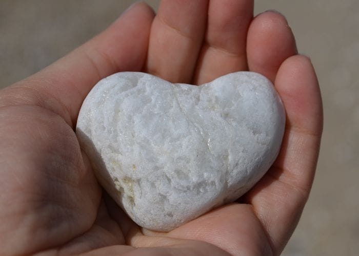 Hand gifting a white stone shaped like a love heart show the gift giver love language.