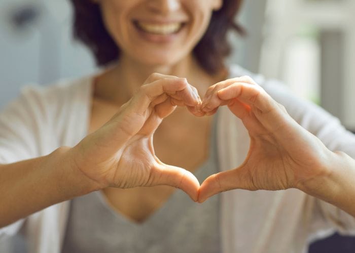 Lady holding her hands in the shape of a heart toward the camera showing her love toward another