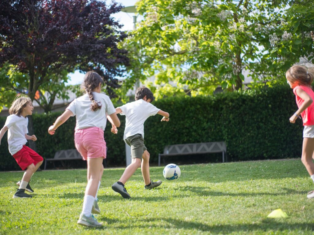 Group of four children playing in the backyard kicking around a ball in a soccer activity.