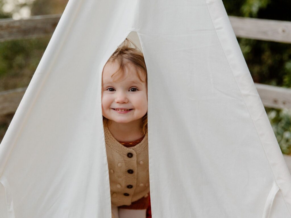 White fabric hut set up outside with a little girl popping her head out the door.