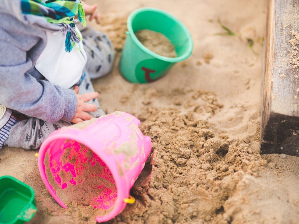 Young child sitting in a sandpit with two buckets doing a sand play activity.