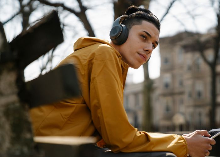 Teen boy sitting on a bench seat leaning on his elbows with headphone on and holding a phone