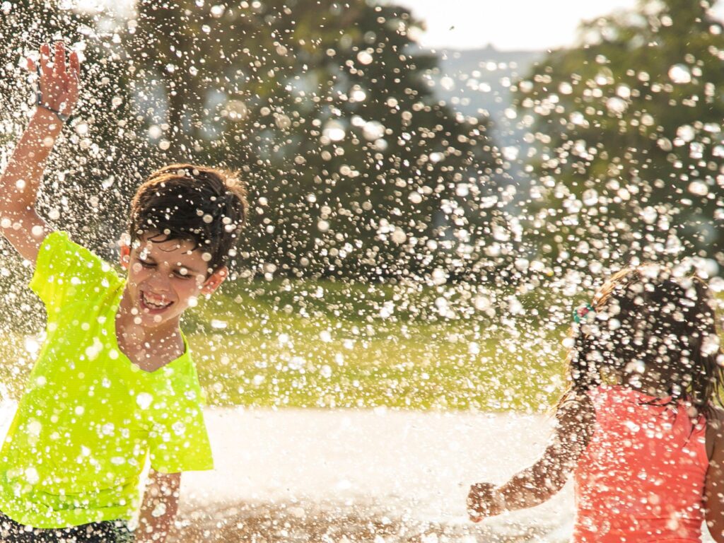A boy and a girl playing in the water from a garden sprinkler in their yard, a great screen free activity for kids.