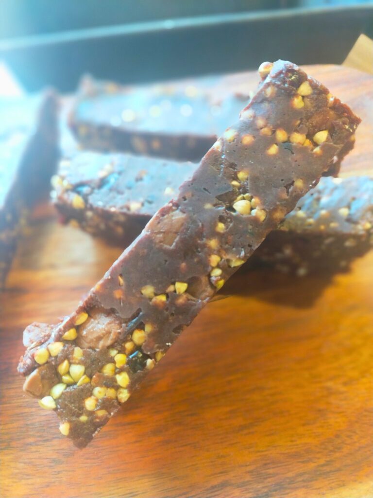 A slice of no bake energy bar sitting on a wooden board with the rest of the slices behind.