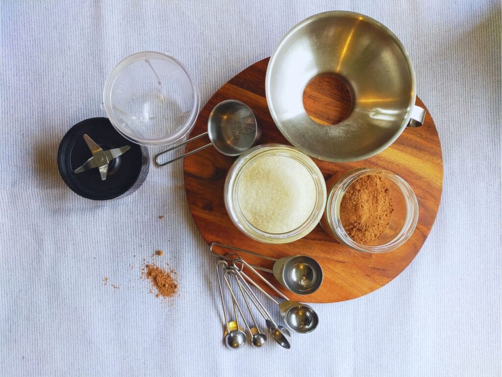 Ingredients and tools needed to make hot chocolate powder sitting on a wooden board on a blue and white table cloth