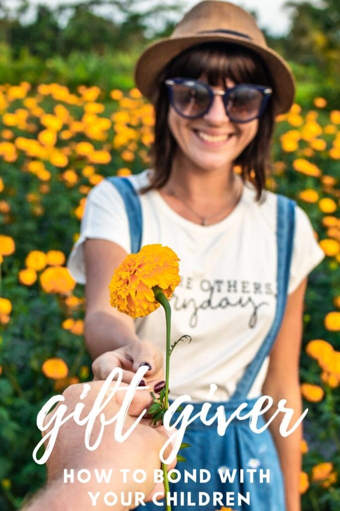 PIN gift giver love language - handing a young lady an orange flower while she is standing in a field of flowers.