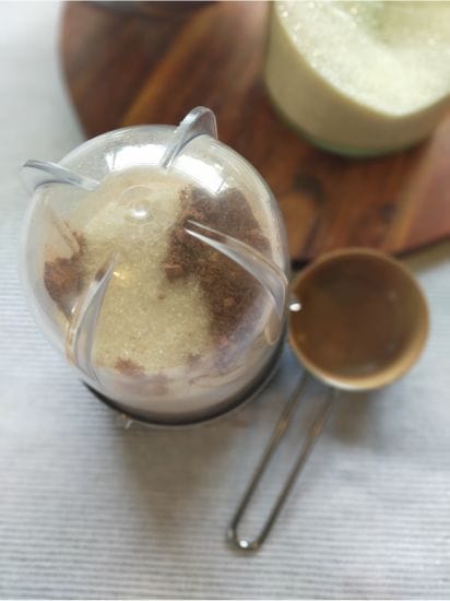 magic bullet with hot chocolate powder ingredients inside sitting on a table next to a wooden board and a measuring cup