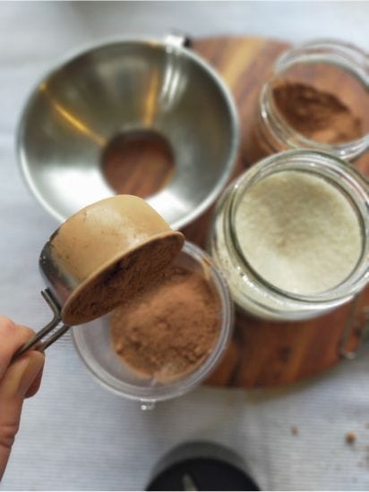 Pouring cacao powder into the magic bullet ready to blend