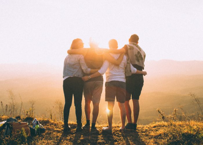 group of people hugging at the top of a mountain at sunset