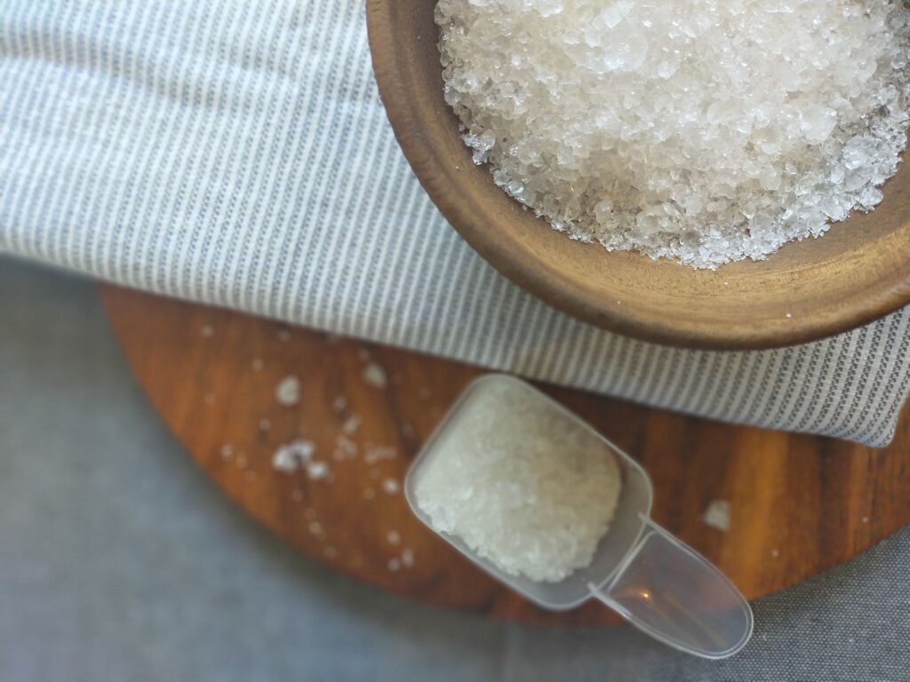 Washing soda in a wooden bowl sitting on a towel next to a scooper